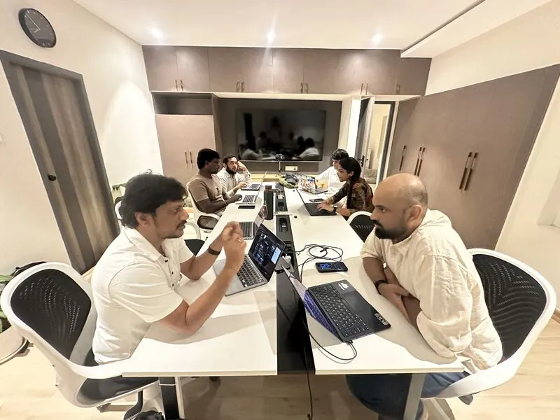 People at a white table with laptops in a small meeting room