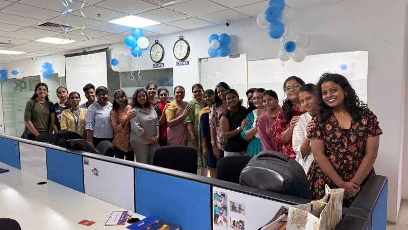 A group of around twenty women standing together in an office decorated with blue balloons